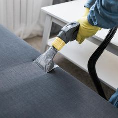 a person using a vacuum to clean a couch with a blue cover and yellow gloves