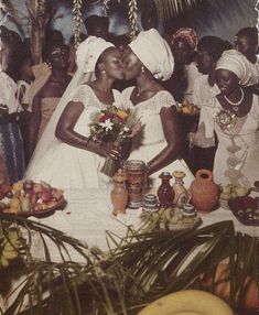 two brides kissing in front of a table full of fruit and other foods on it