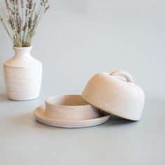 two white dishes sitting on top of a table next to a vase