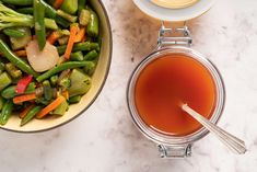 a bowl of stir fried vegetables next to a cup of tea on a marble table