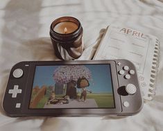 a nintendo wii game system sitting on top of a bed next to a candle and book