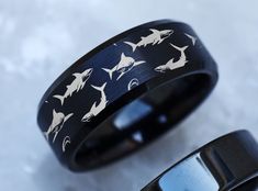 two black rings with white sharks on them, one is in the process of being engraved