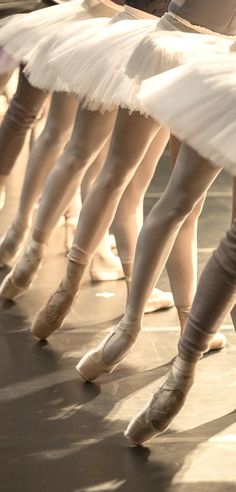 several ballerinas in white tutus and ballet shoes are lined up on the floor