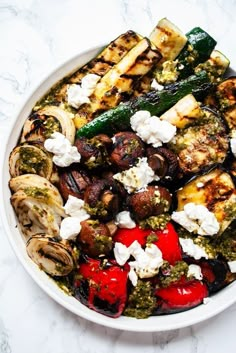 a white bowl filled with grilled vegetables and feta cheese on top of it