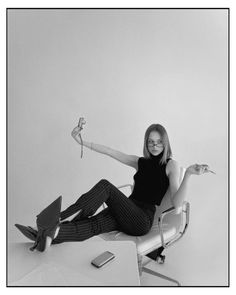 a woman sitting in a chair with her legs crossed and holding a flower up to the side