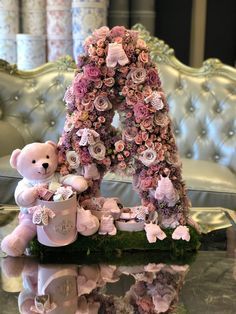 a teddy bear sitting on top of a table next to a letter made out of flowers