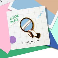 a hand holding a magnifying glass with the words look into enamel pins on it