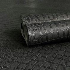 two rolls of black leather sitting on top of a tablecloth covered surface with an embossed pattern