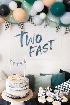 there is a cake and cupcakes on the table in front of some balloons