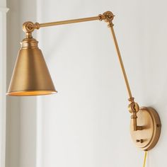 a wall light with a gold shade on it next to a white wall and window