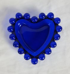 a blue heart shaped brooch sitting on top of a white cloth