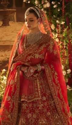 a woman in a red and gold bridal gown standing next to flowers with her hands on her hips