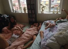 three people laying in bed with books on the windowsill and one person lying down