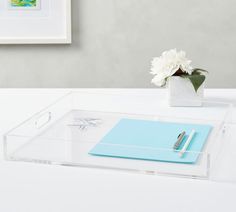 a clear desk with a pen, notepad and flower on it next to a white wall