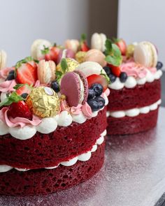 two red velvet cakes with white frosting and fruit toppings on each cake stand