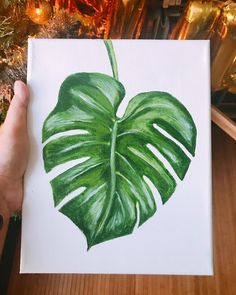 a hand holding up a green leaf on a white paper in front of a christmas tree