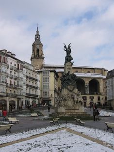 a statue in the middle of a plaza with snow on the ground and people walking around