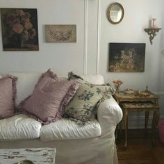 a white couch with pillows on it in a living room next to a table and mirror