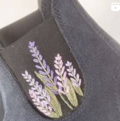 a pair of gray shoes with purple and green flowers embroidered on the side of them