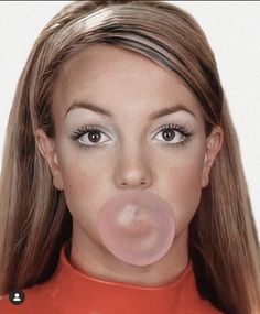 a woman with long blonde hair blowing a bubble on her nose while wearing a red shirt