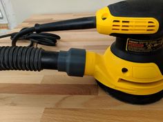 a yellow and black sander sitting on top of a wooden table next to a power cord