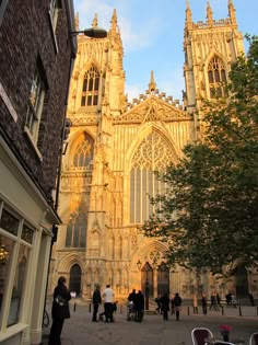 people are walking around in front of a large building with many windows and tall spires