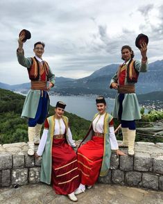 three people dressed in traditional clothing posing for a photo on top of a hill overlooking a lake