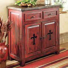 a wooden cabinet sitting on top of a rug next to a vase with flowers in it