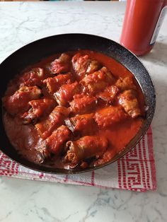 a skillet filled with meat and sauce on top of a table next to a drink