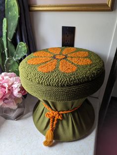 a green cushion with an orange flower on it sitting next to a pink flower vase