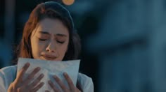 a woman holding a piece of white paper in her hands while looking at the screen