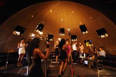 a group of people standing around each other in a room with lights on the ceiling