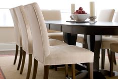 a dining room table with white chairs and a bowl of fruit on top of it