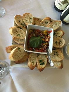 a table topped with bread slices and a bowl filled with food next to two bottles of wine