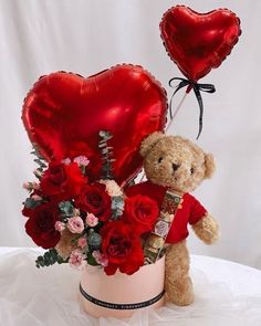 a teddy bear sitting on top of a table next to a bouquet of roses and heart shaped balloons