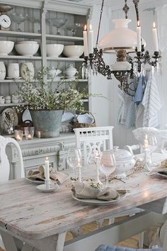 a dining room table with white chairs and plates on it, in front of a china cabinet