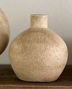 two white vases sitting on top of a wooden table next to each other in front of a wall