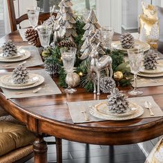 a dining room table set for christmas with pine cones and silver ornaments on the placemats