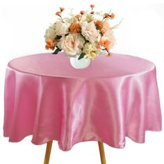 a pink table cloth with flowers in a vase on it and an empty chair underneath