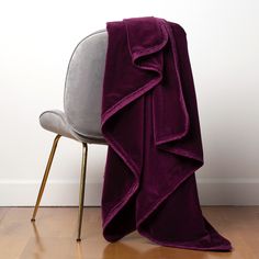 a purple blanket sitting on top of a chair next to a white wall and wooden floor