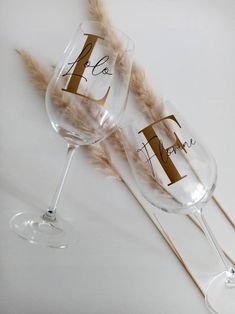 two wine glasses sitting next to each other on top of a white table with feathers