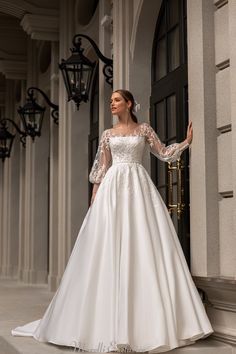 a woman in a white wedding dress standing by a door with her hands on her hips