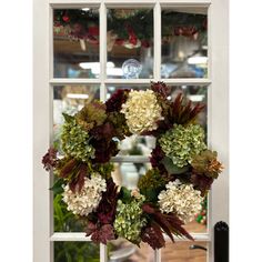 a wreath hanging on the front door of a house with white and green flowers in it