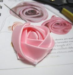 a pair of scissors and some pink flowers on top of a piece of paper with ribbon