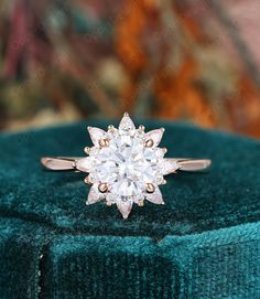 an engagement ring sitting on top of a green velvet covered cushioned surface, with the center diamond surrounded by smaller round diamonds