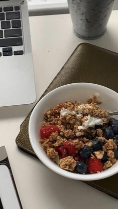 a bowl of granola with yogurt and berries in front of a laptop