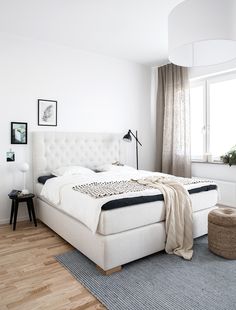 a white bed sitting next to a window in a bedroom on top of a hard wood floor