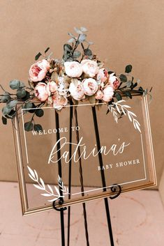 a welcome sign with flowers and greenery is displayed on a metal easel for an outdoor wedding