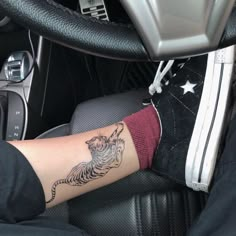 a person with a tiger tattoo on their arm sitting in a car seat next to a steering wheel