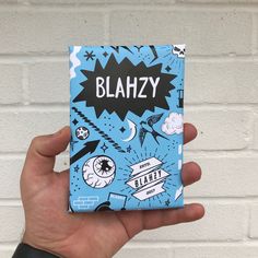 a person holding up a book with the word blahzy on it in front of a white brick wall